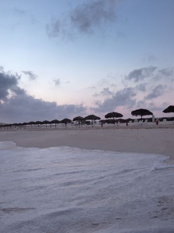 Strand bei Sonnenuntergang mit Schirmen und sanften Wellen