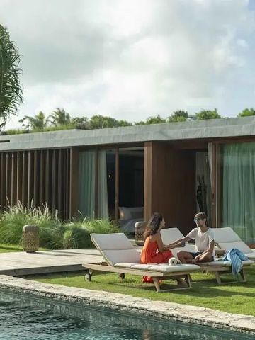 Paar entspannt auf Liegestühlen am Pool vor moderner Villa mit tropischem Garten