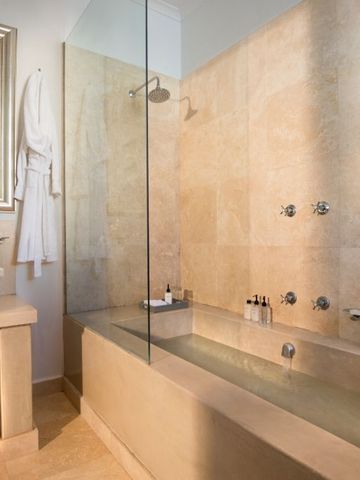 Luxuriöses Badezimmer mit Natursteinbadewanne und Glasdusche.