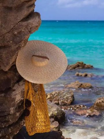 Strand mit Felsen und türkisblauem Meer, Strohhut hängt an Felsen