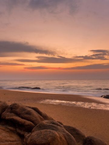 Sandstrand bei Sonnenuntergang mit ruhiger Meeresbrandung.