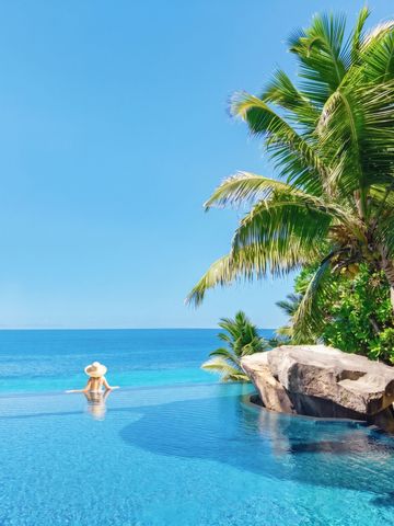 Person im Infinity-Pool mit Blick auf das kristallklare Meer im Cheval Blanc Seychelles