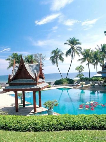 Tropische Poollandschaft mit Meerblick und traditionellen Pavillons umgeben von Palmen