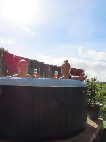 Zwei Personen genießen einen Whirlpool mit Blick auf grüne Wiesen bei Sonnenschein.