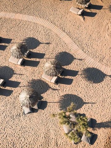 Luftbild von Strand mit Sonnenschirmen und Liegen auf Sand.