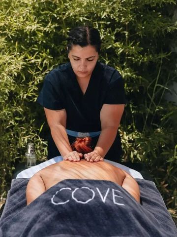Wellnessmassage auf einem Tisch im Freien unter grünem Laub.