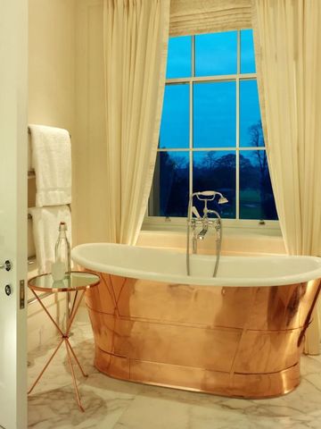 Luxuriöses Bad mit freistehender Kupferbadewanne vor Fenster