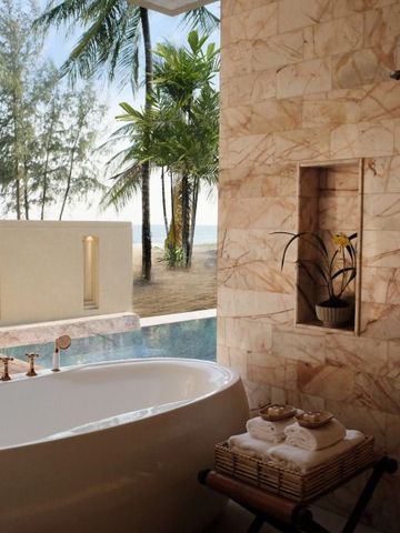 Außenbereich mit Badewanne, Pool und Blick auf Palmen und Meer.
