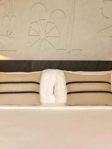 Doppelbett mit dekorativen Kissen und kunstvoller Wandverzierung im Hotelzimmer.