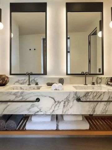 Modernes Badezimmer mit Doppelwaschbecken aus Marmor und beleuchteten Spiegeln.