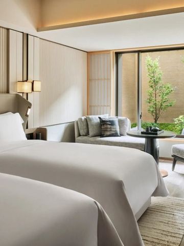 Hotelzimmer mit zwei Betten und gemütlicher Sitzecke mit Blick auf einen Garten