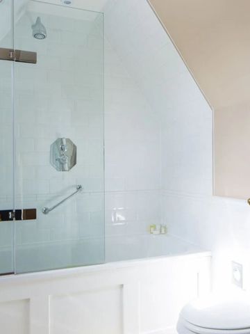 Helles Badezimmer mit moderner Badewanne und Glasduschwand unter Dachschräge