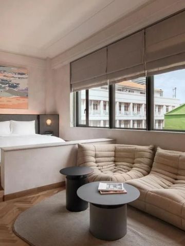 Hotelzimmer mit modernem Sofa, großem Fenster und einem Kunstwerk über dem Bett.