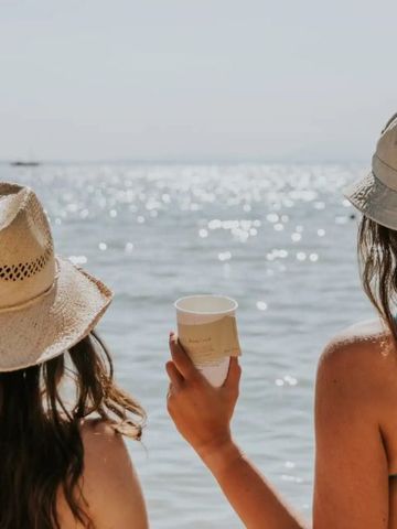Zwei Personen am Strand mit Sonnenhüten Blick auf das Meer genießend