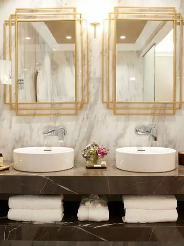 Modernes Badezimmer mit Doppelwaschbecken und goldenen Spiegeln.