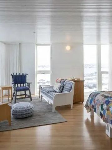 Helles Zimmer mit großem Fenster, Sofa und Bett mit farbiger Decke.