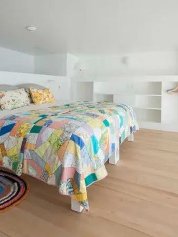 Minimalistisches Schlafzimmer mit hellem Holzfußboden und bunter Tagesdecke.