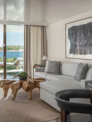 Elegantes Wohnzimmer einer Suite mit Holz-Couchtisch, hellem Sofa und Meerblick durch große Glasfront.