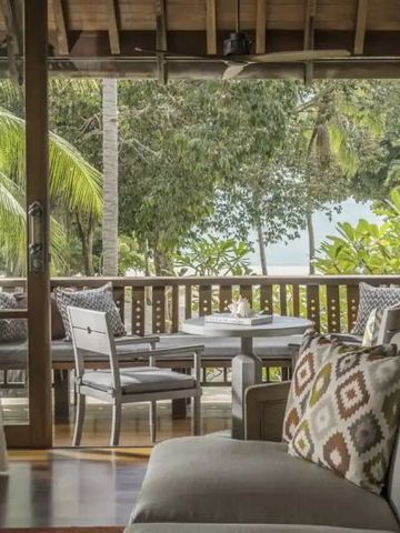 Sitzbereich mit Blick auf Palmen und Meer durch Balkon im Hotelzimmer