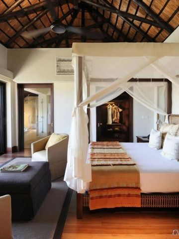 Geräumige Suite im Four Seasons Safari Lodge mit Himmelbett und Strohdach.