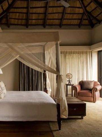 Elegantes Schlafzimmer mit großem Himmelbett und Panoramafenster im Four Seasons Safari Lodge.