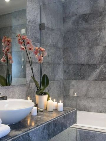 Modernes Badezimmer mit Blumen und Kerzen auf grauem Steintisch