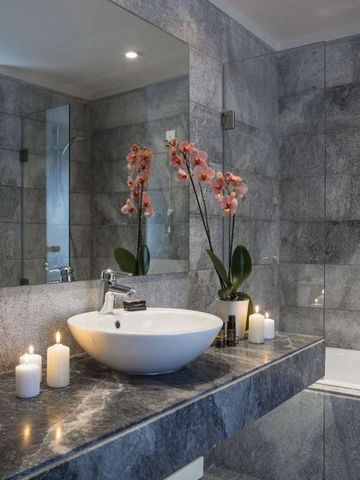 Elegantes Badezimmer mit grauen Steinfliesen und weißen Waschbecken, dekoriert mit Orchideen