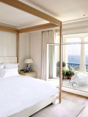Helles Schlafzimmer mit Himmelbett und Meerblick durch geöffnete Glastür