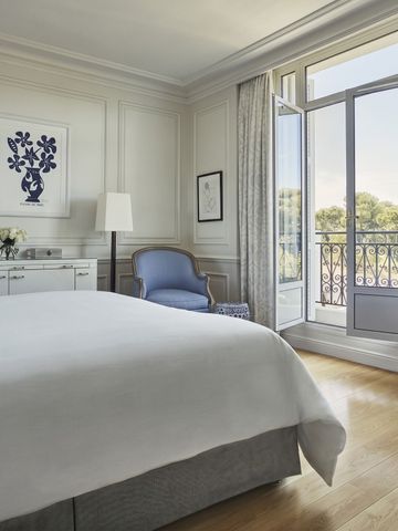 Elegantes Hotelzimmer mit Balkonblick auf Bäume und französischen Türen.