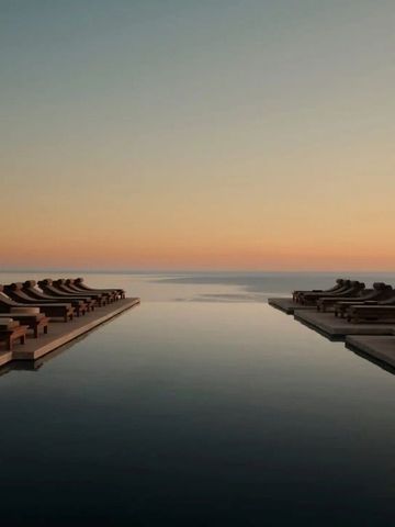 Infinity Pool mit Liegestühlen und atemberaubendem Sonnenuntergang über dem Meer