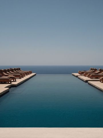 Infinity Pool mit Liegestühlen unter klarem Himmel und Blick auf das weite Meer