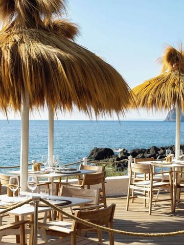 Strandterrasse mit strohbedeckten Sonnenschirmen und Blick aufs Meer