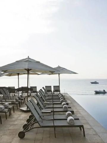 Liegen und Sonnenschirme am Infinity-Pool mit Blick aufs Meer bei Sonnenaufgang