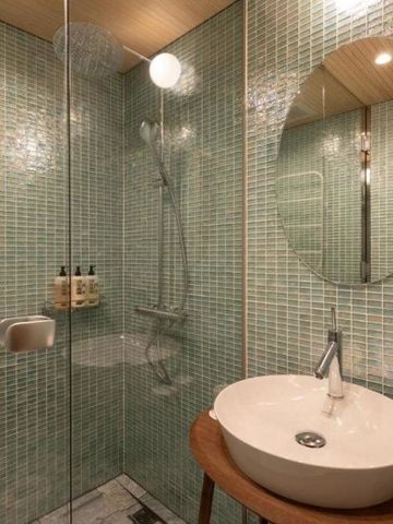 Badezimmer mit gläserner Dusche und grünen Fliesen