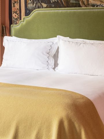 Bett mit grüner Kopfstütze und gelber Decke vor dekorativer Wand