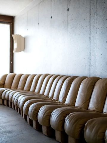 Lange braune Ledercouch in minimalistischem Raum mit Betonwand.