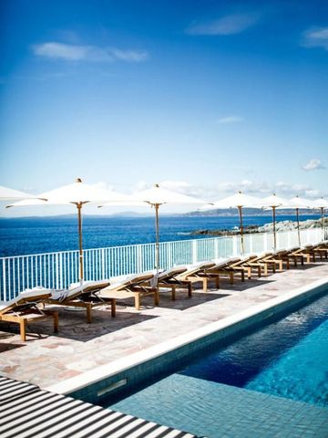 Pool mit Liegestühlen und Sonnenschirmen vor Meerblick.
