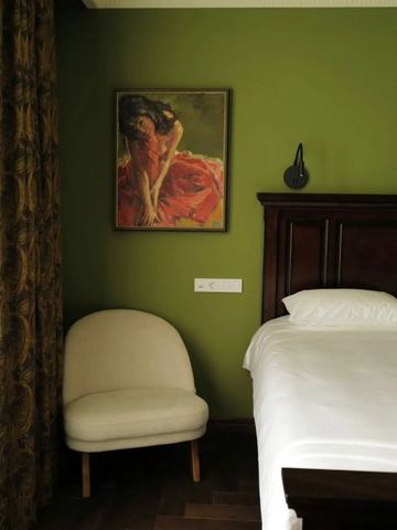 Hotelzimmer mit grün gestrichenen Wänden und Kunstwerk über einem luxuriösen Bett