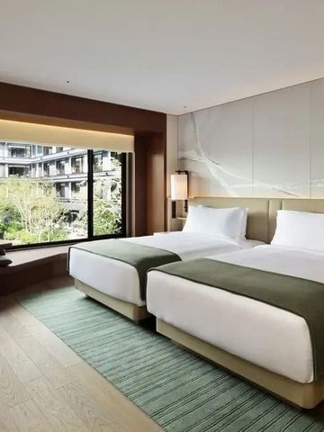 Modernes Hotelzimmer mit zwei Betten und Blick ins Grüne.