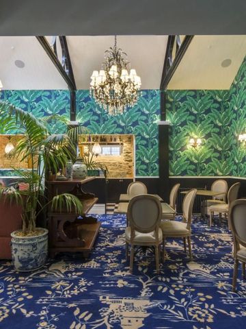 Stilvoll dekorierte Lounge mit Palmentapete, Kronleuchter und eleganten Stühlen