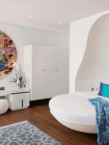 Geräumiges Schlafzimmer mit rundem Bett und farbenfrohem Kunstwerk an der Wand.