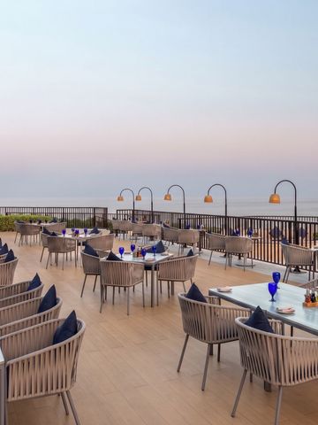 Terrasse mit Esstischen und Blick aufs Meer bei Sonnenuntergang