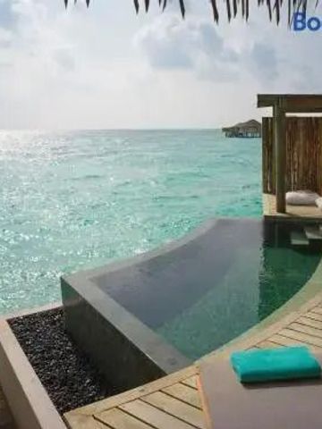 Infinity-Pool mit Blick auf das türkisfarbene Meer und hölzerner Terrasse.