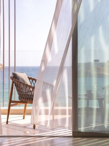 Balkon mit Meerblick durch leichte Vorhänge und bequemer Sitzgelegenheit.
