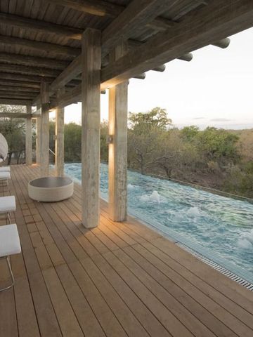 Infinity-Pool mit Holzterrasse und Liegestühlen in natürlicher Umgebung