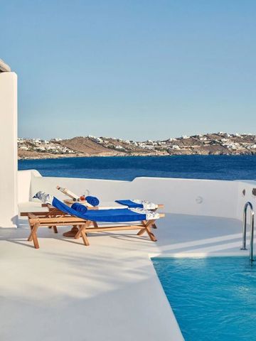 Sonnenliegen mit blauen Kissen am Pool mit Blick auf das Meer und die Hügel von Mykonos