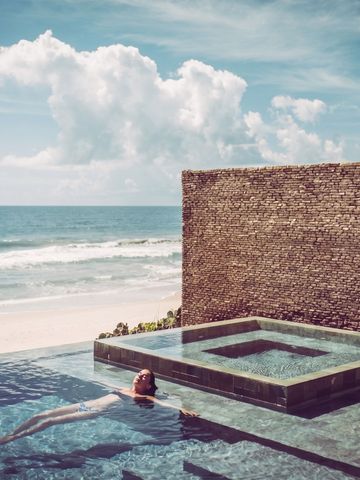 Infinity-Pool am Strand mit schwimmender Person und klaren Himmel