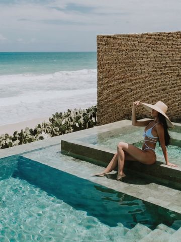 Frau in Bikini und Hut am Rand eines Infinity-Pools mit Meerblick