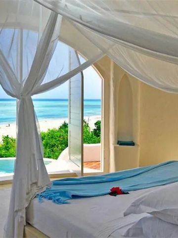 Bett mit Meerblick durch offene Fenster mit weißen Vorhängen drapiert