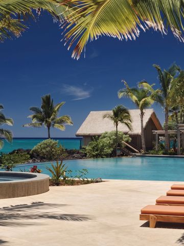 Poollandschaft mit Palmen und traditionellen Strohhütten am Meer